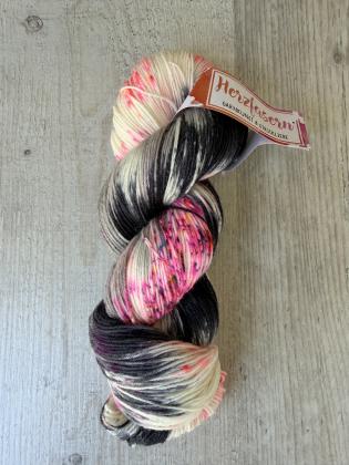Handgefärbter Wollstrang „Mitternachtsfunken“ auf Herzfasern No. 20. Die Färbung kombiniert dunkle Anthrazit- und Schwarztöne mit naturweißen Bereichen und leuchtenden Neonpink-Sprenkeln.